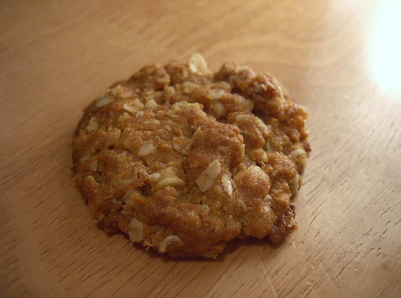 A single golden-brown Anzac biscuit with an oat-flecked surface on a wooden table photo_0 A single golden-brown Anzac biscuit with an oat-flecked surface on a wooden table photo_0