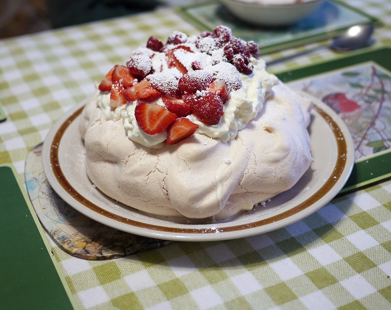 A large pavlova on a plate with a cracked meringue shell, whipped cream, sliced strawberries and raspberries dusted with icing sugar photo_0