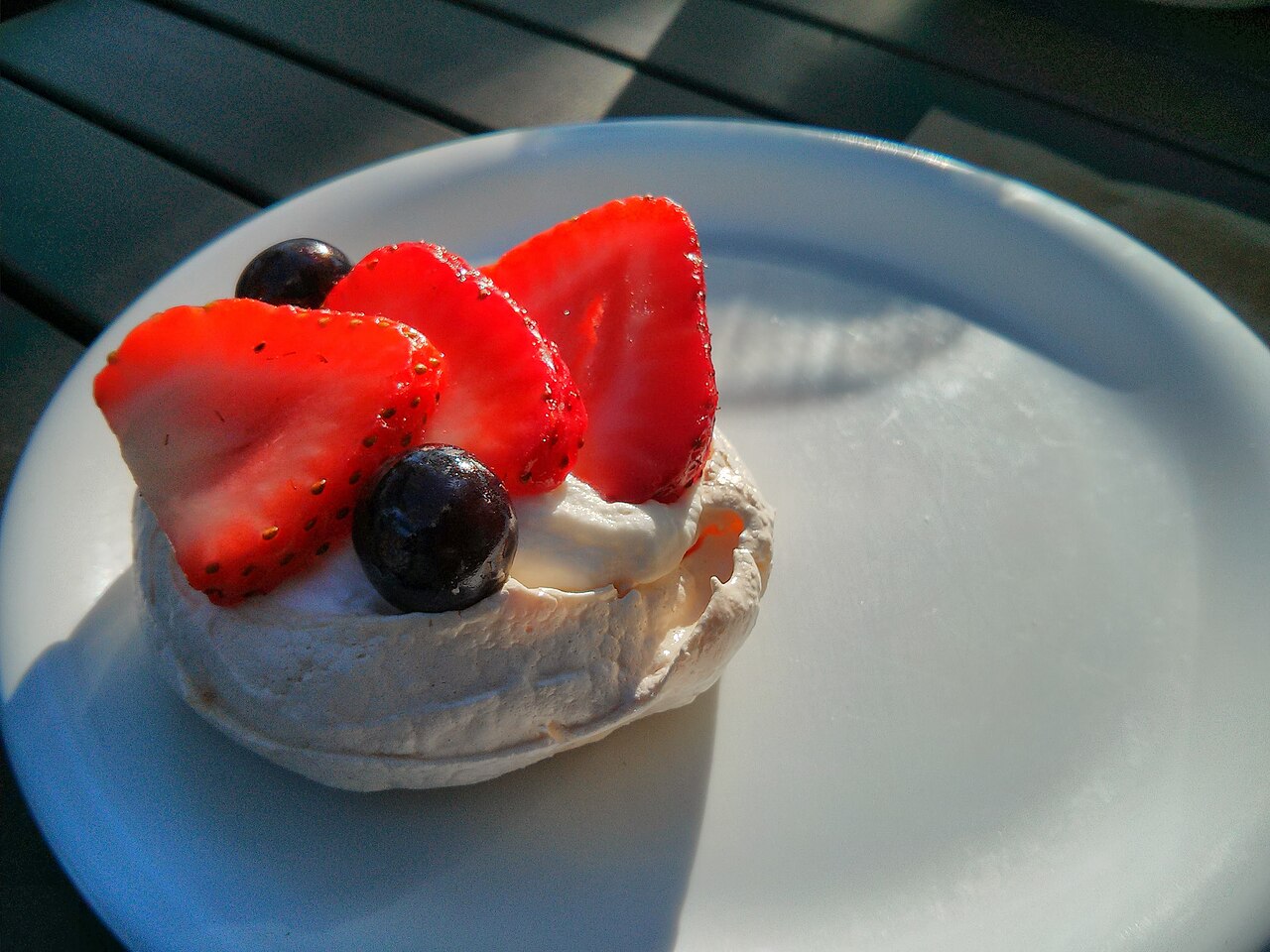 A small individual pavlova with whipped cream, sliced strawberries and blueberries on a white plate photo_0